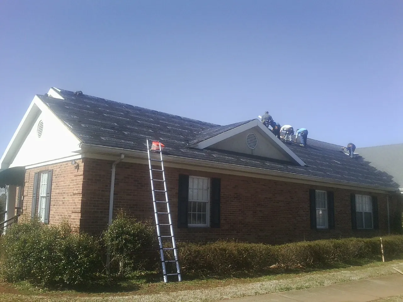 Crew tearing shingles off a brick ranch roof with a ladder set — Emergency Roof Repair work by our crew in Salt Lick