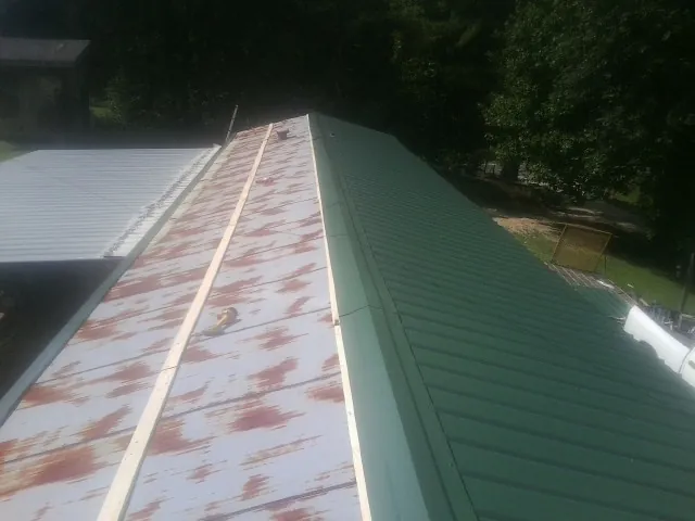Old rusted panels beside newly installed green metal roofing — Wind Damage Roof Repair by Roofing Brothers in Salt Lick