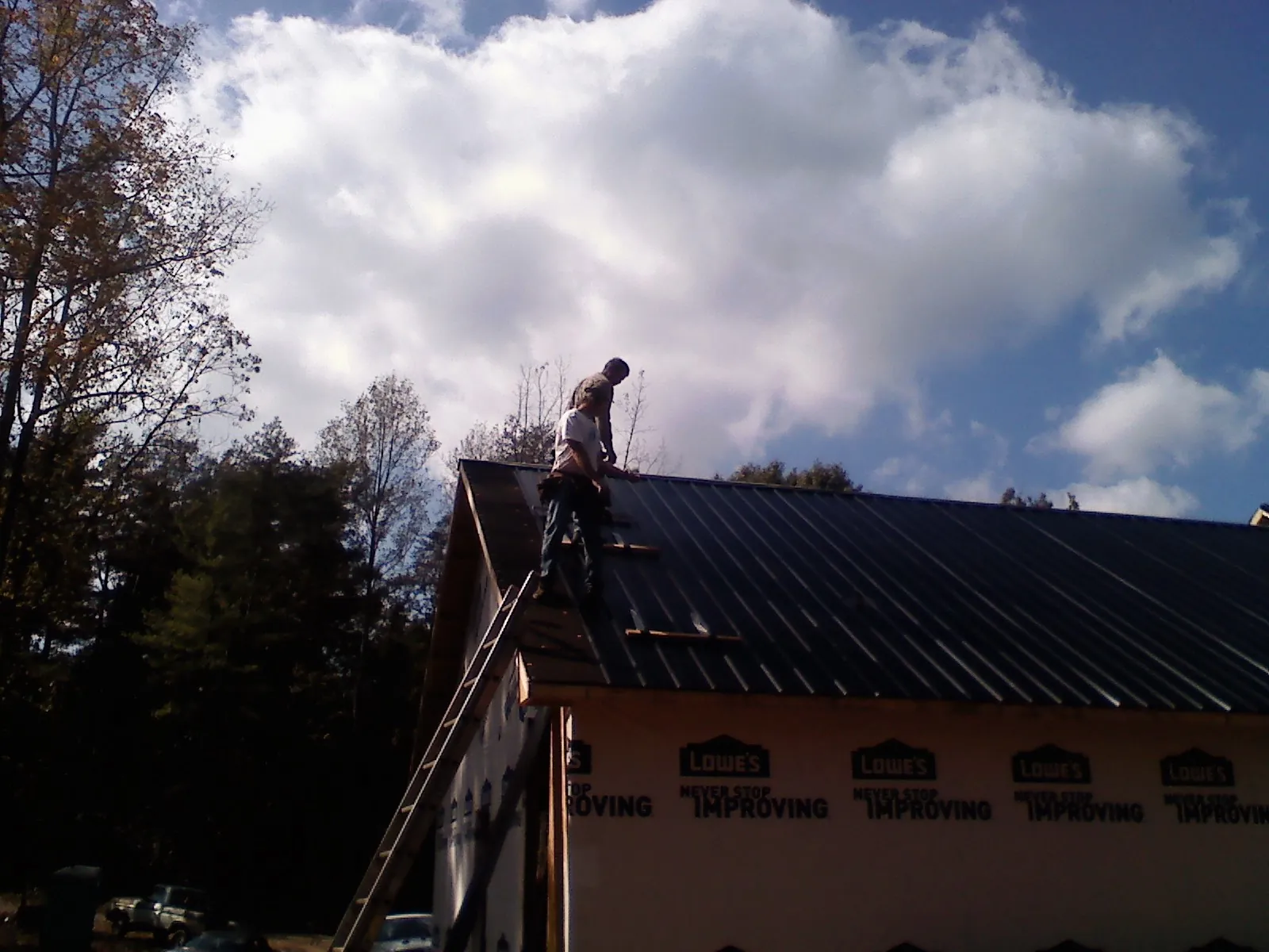Roofer fastening dark metal panels high against a cloudy sky, from a Roof Inspection job in Salt Lick