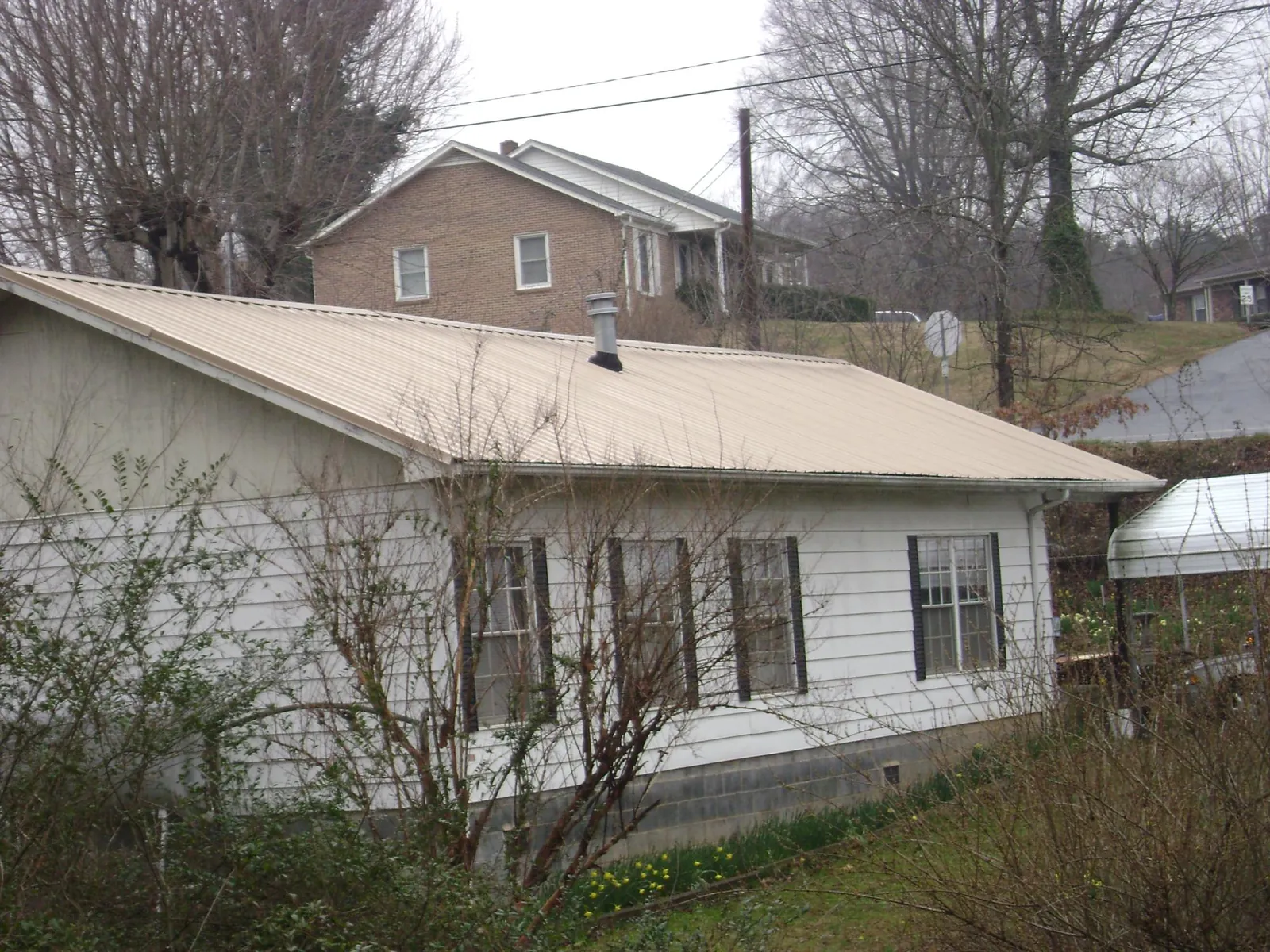 Tan metal roof on a white sided house set into a hillside — Commercial Roofing by Roofing Brothers in Salt Lick