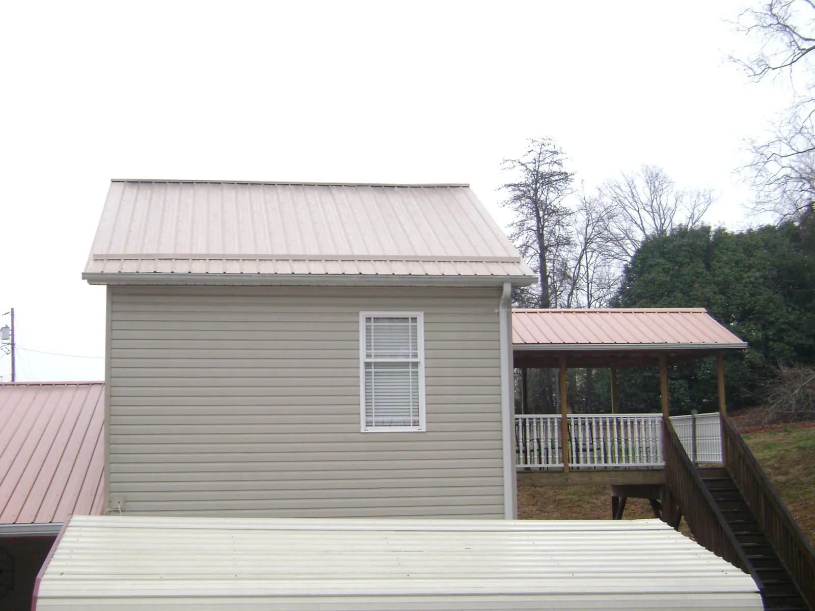 Tan metal roofs on a two story addition and attached porch, from a Roof Replacement job in Salt Lick